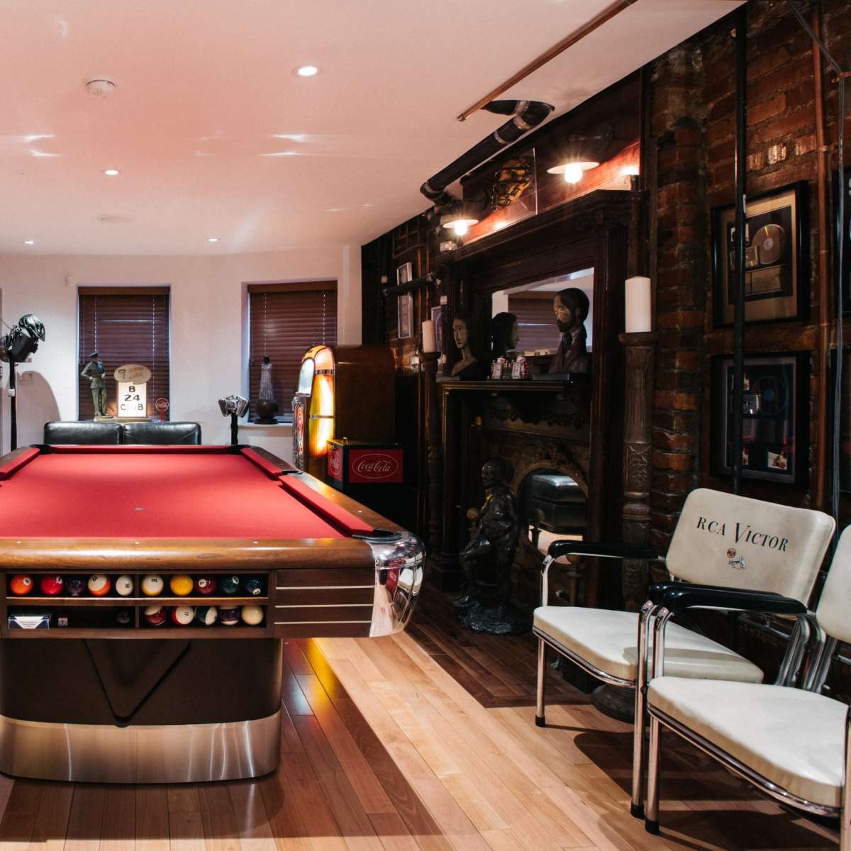 A room featuring a red pool table in the center, surrounded by brick walls, vintage furniture, and various framed photographs and memorabilia.