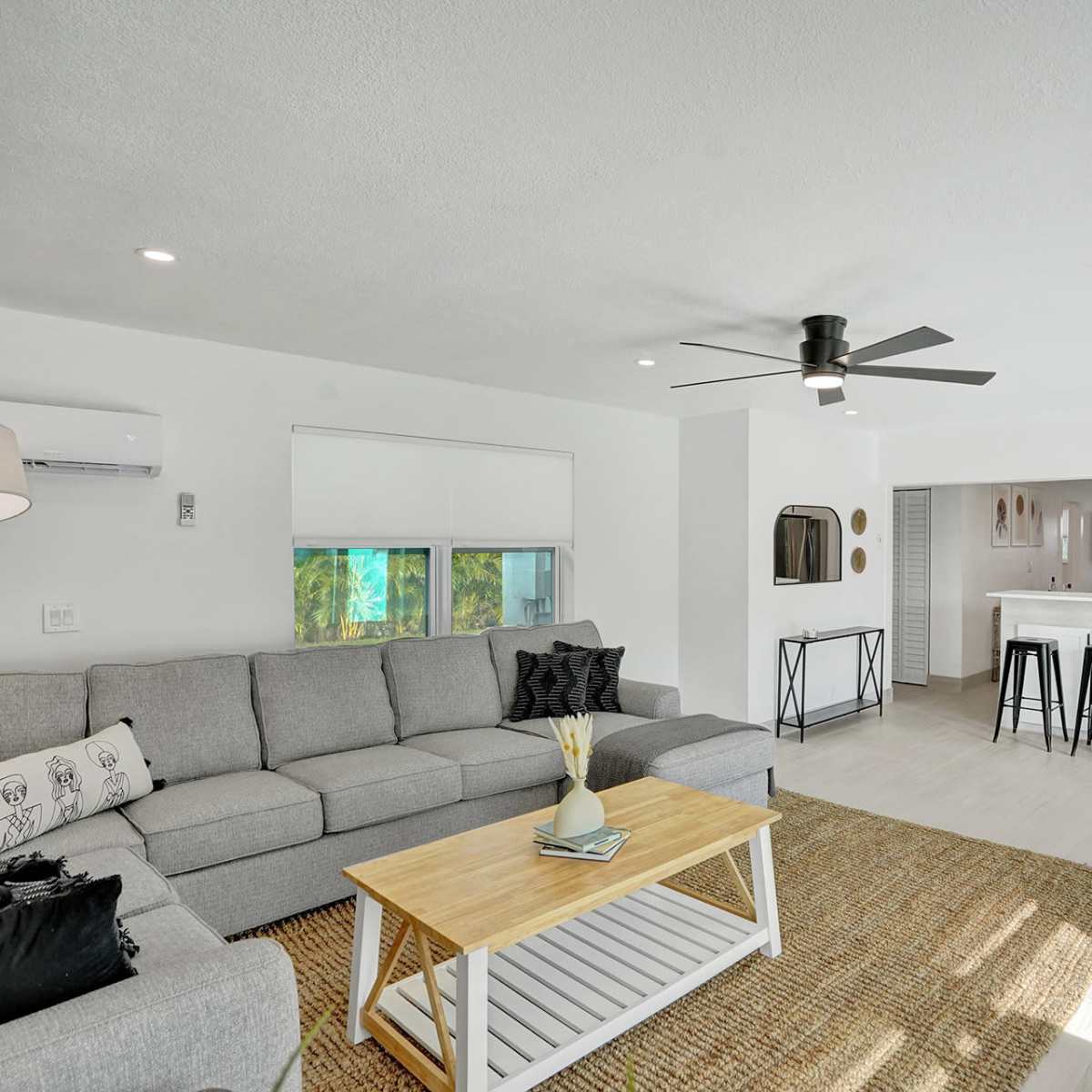 A modern living room with a gray sectional sofa, a wooden coffee table, and a view into a kitchen area with bar seating.