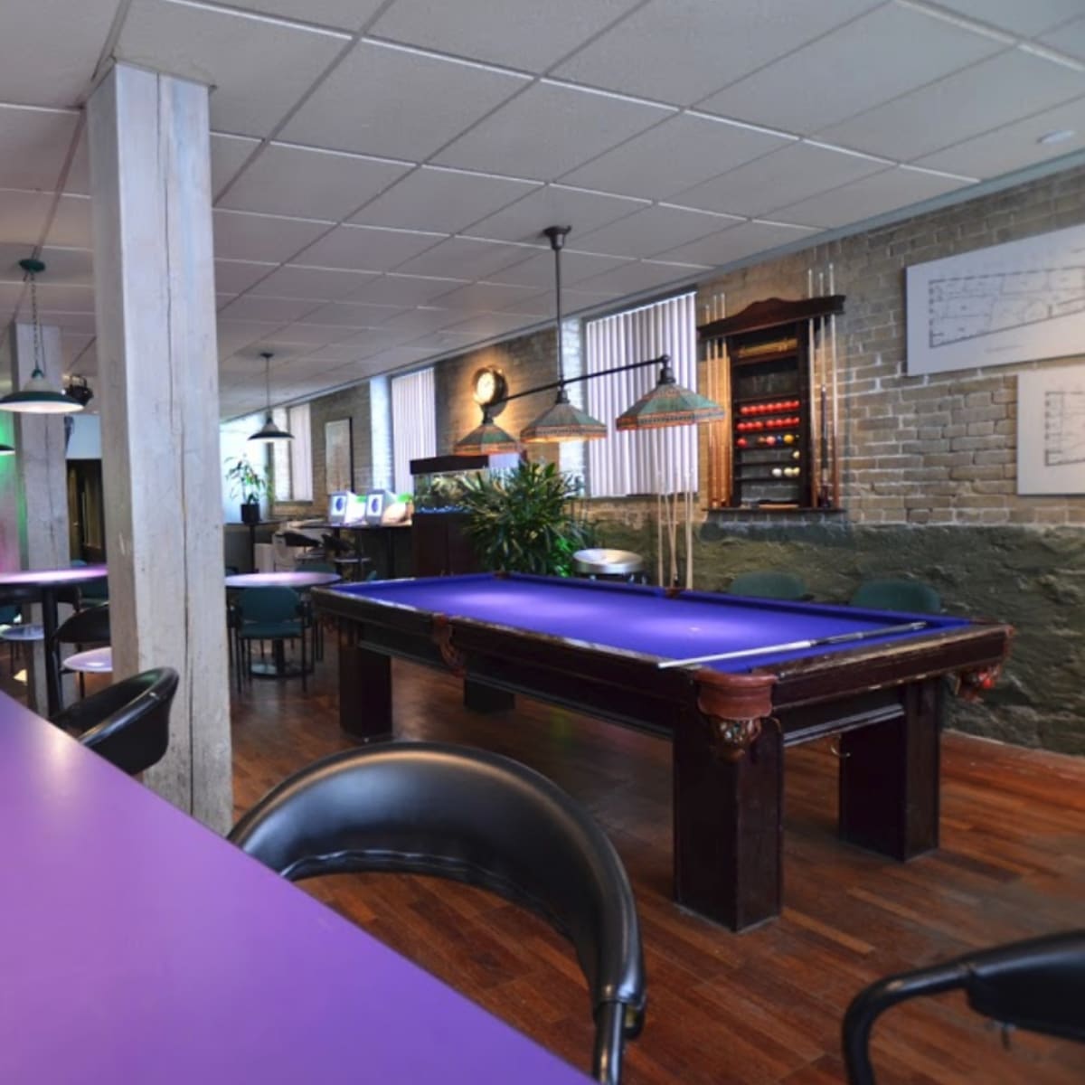 A spacious room featuring a purple pool table, bar counter, and seating areas with ambient lighting.
