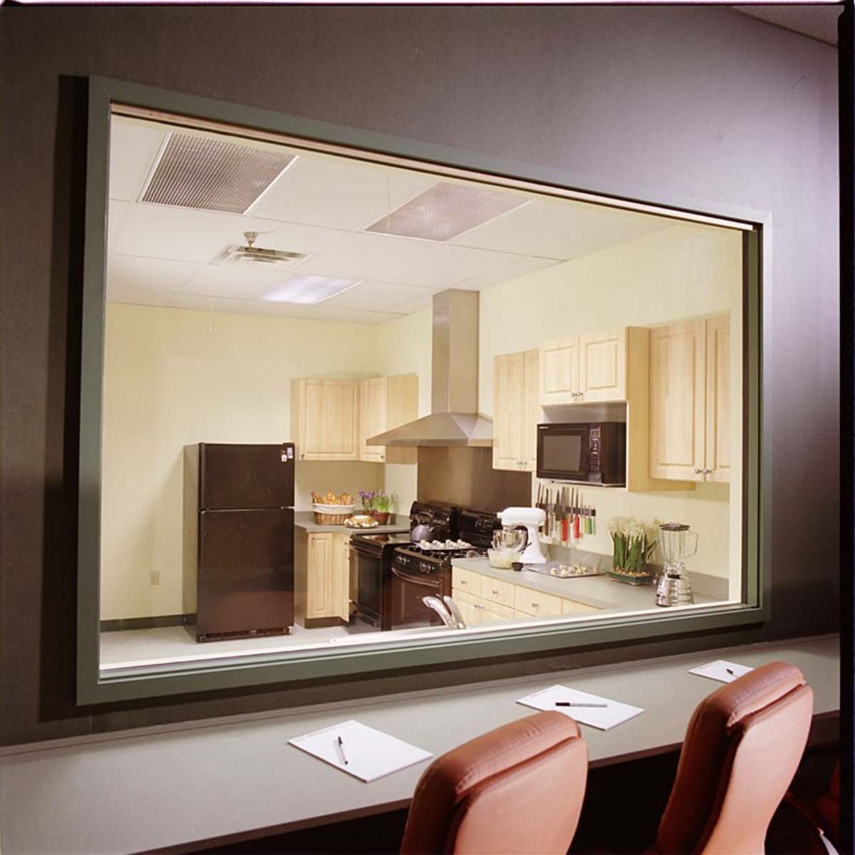 A kitchen visible through a large window, featuring wooden cabinets, appliances, and a countertop with various kitchen items.
