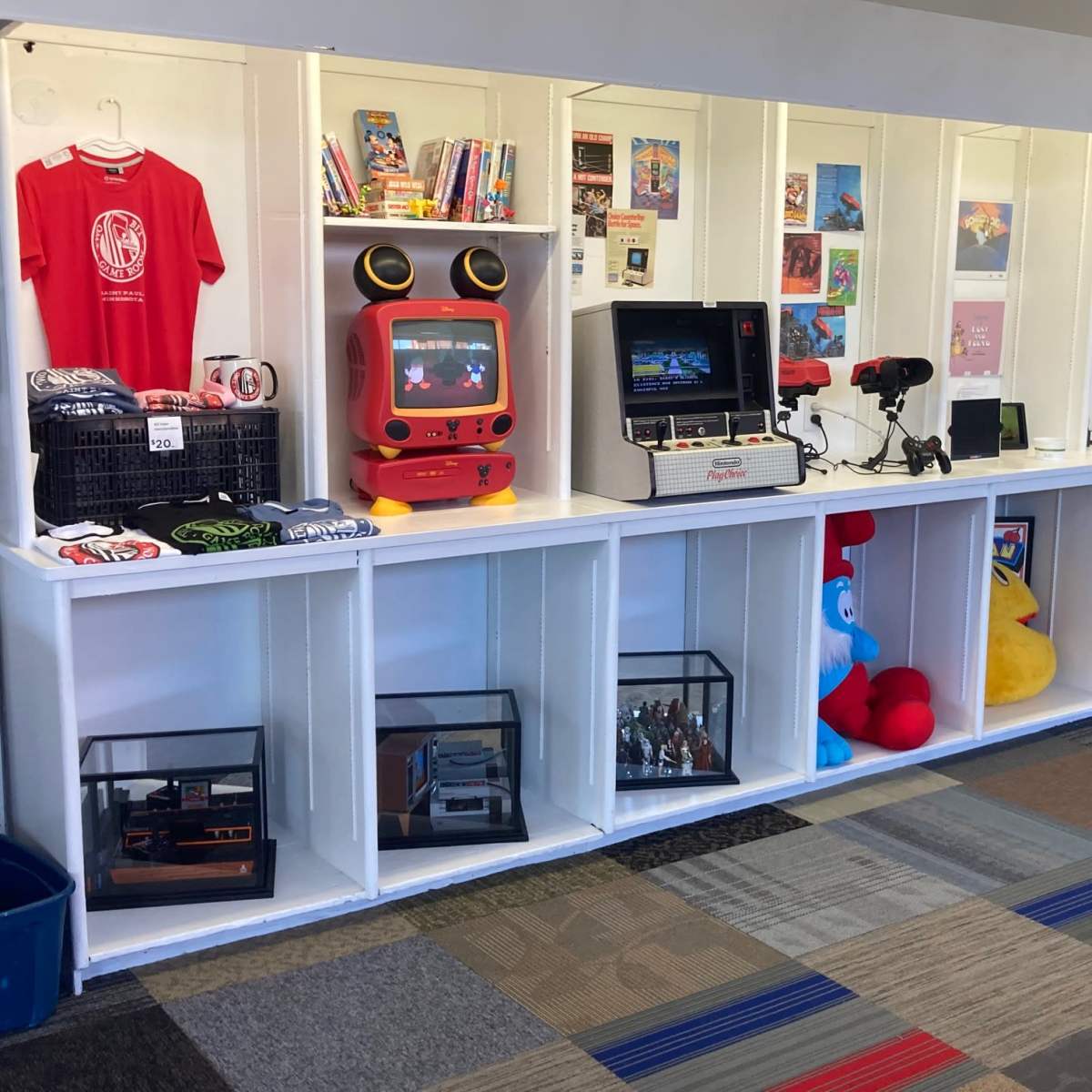A display area featuring vintage arcade games, collectibles, and merchandise, organized on shelves in a brightly lit space.