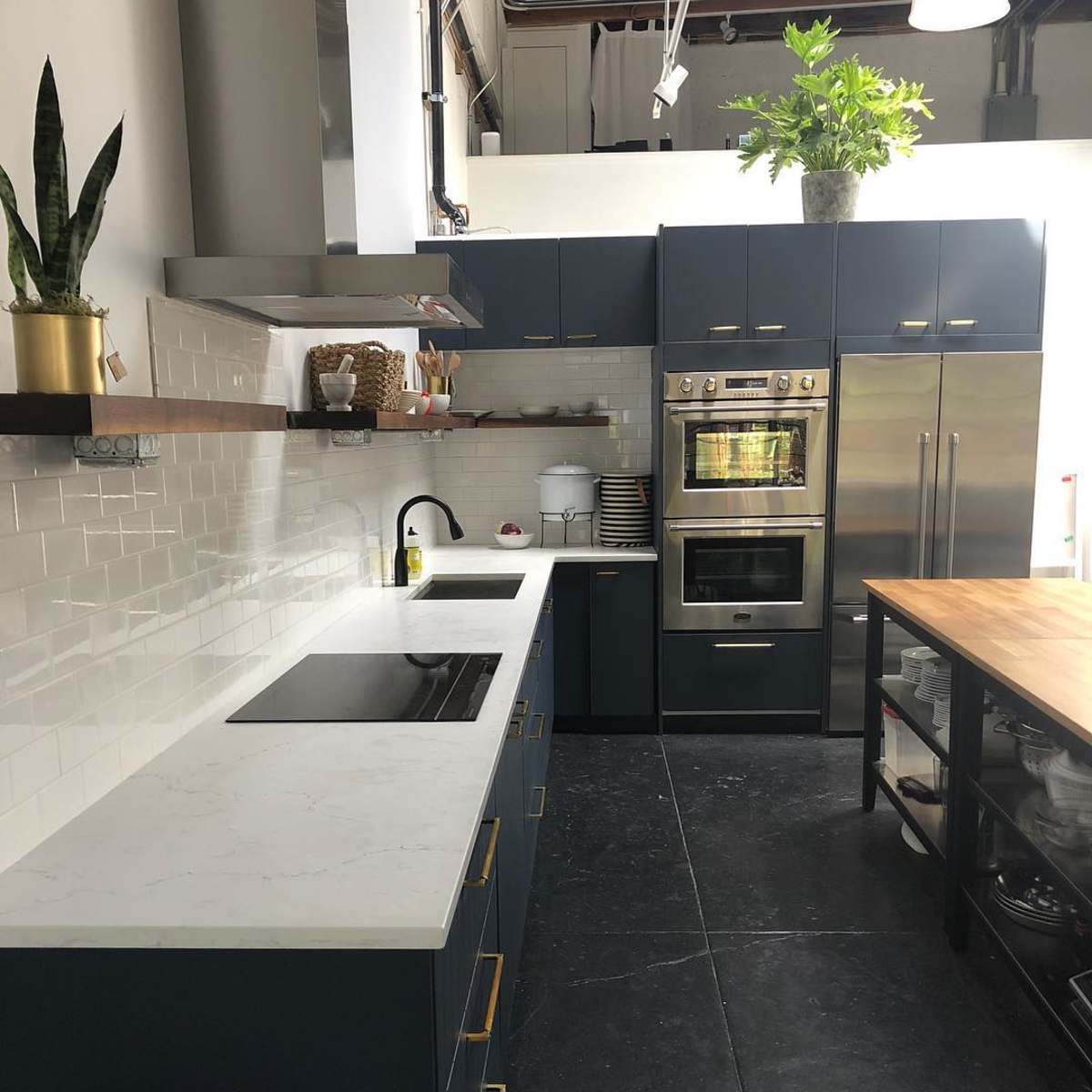 A modern kitchen features dark blue cabinetry, a marble countertop, stainless steel appliances, and an island with open shelving.
