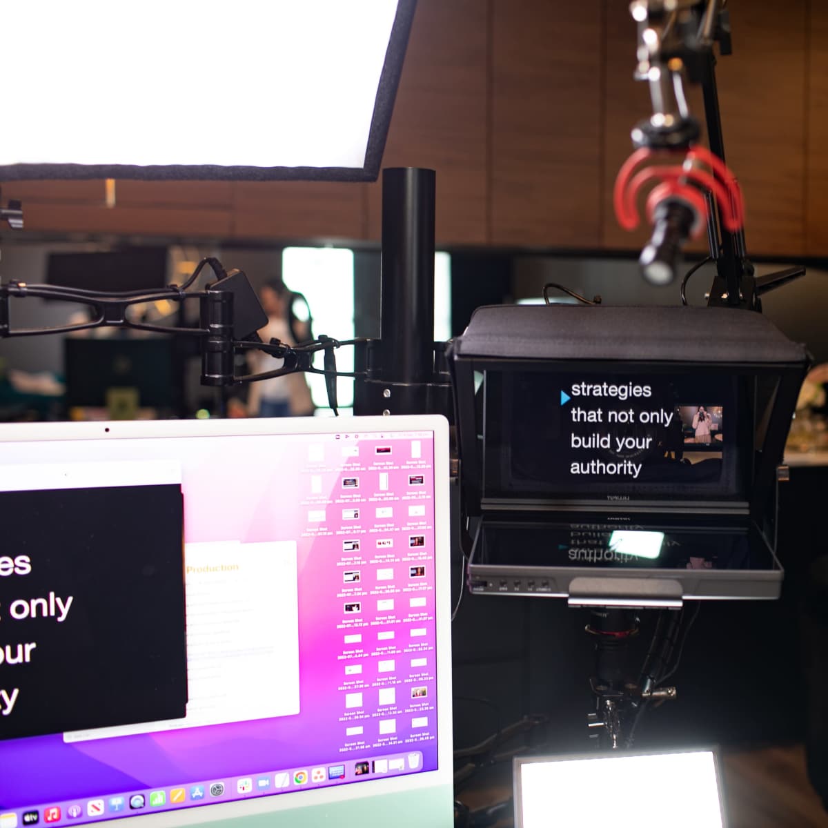 A camera setup displays text on a monitor, with a computer and ring light in the background.