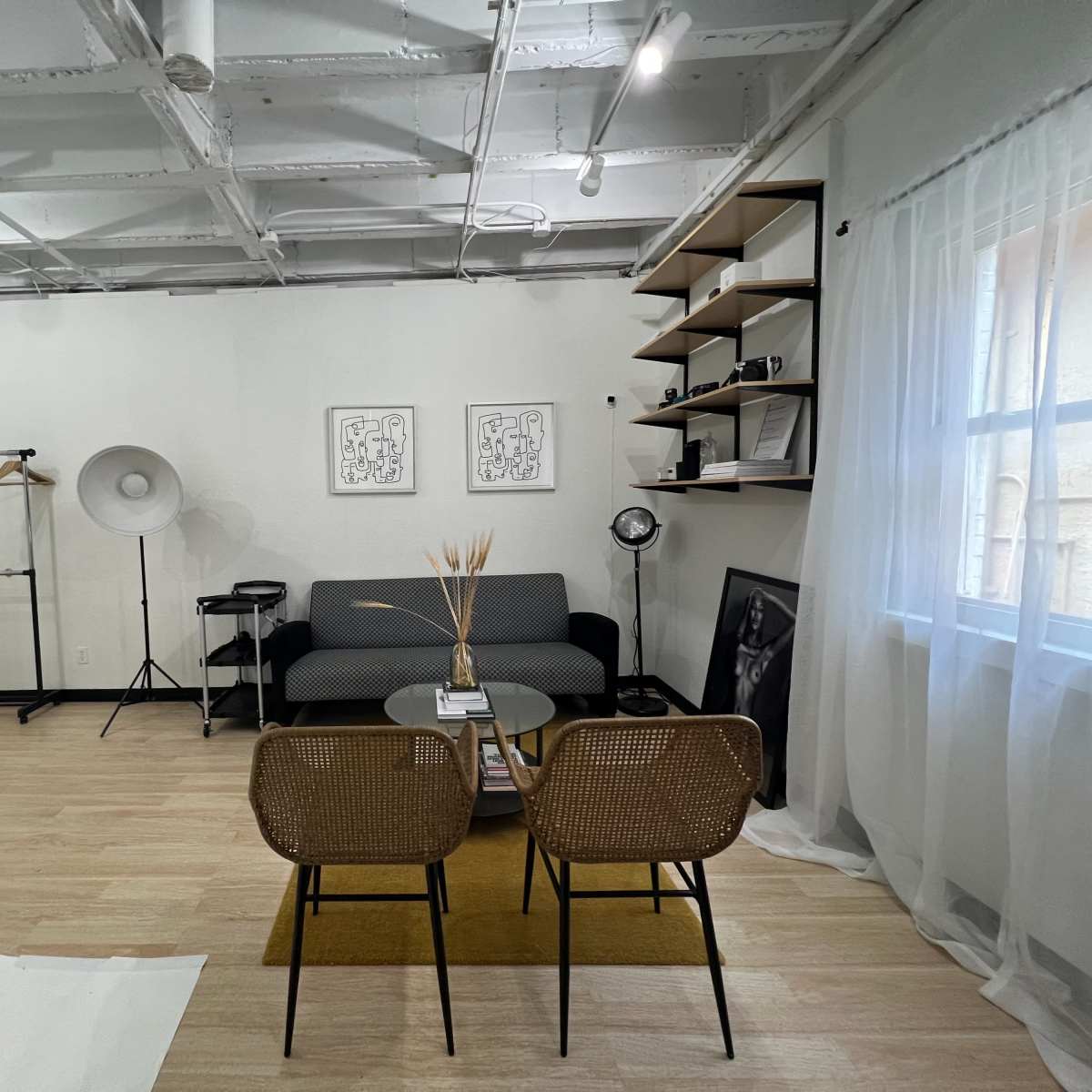 A modern, minimalist room with a gray sofa, two woven chairs, a round coffee table, and decorative elements like a floor lamp and shelving.