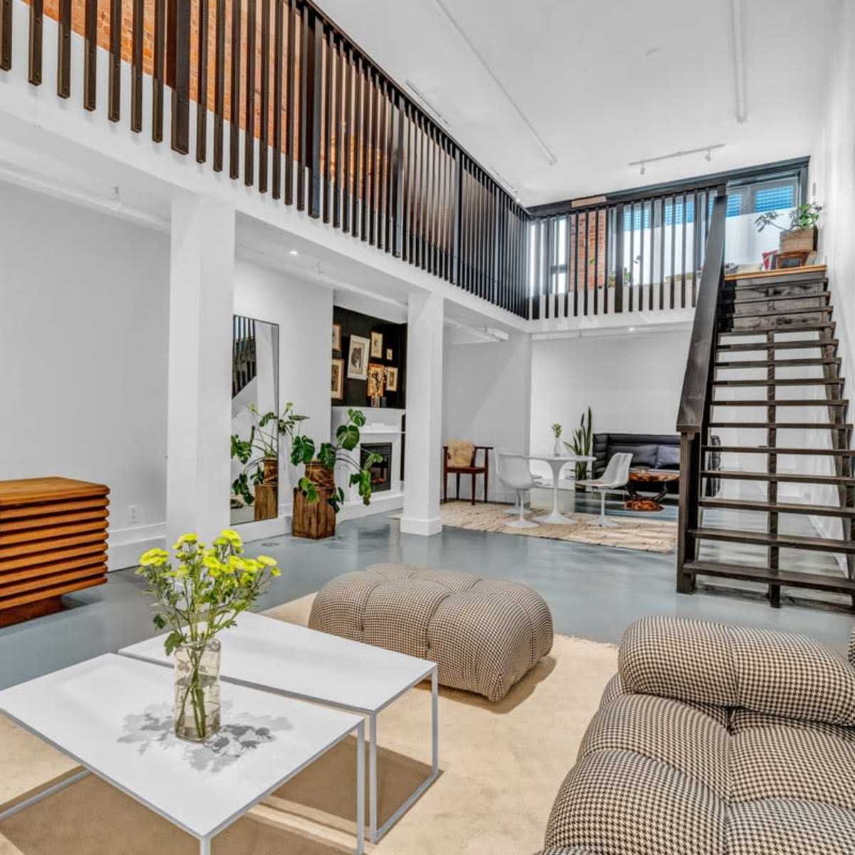 A modern, open-concept living space with a living area, dining area, and a staircase leading to an upper level.