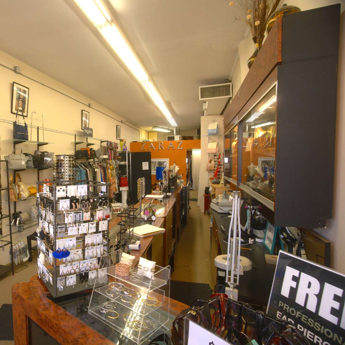 The interior of a retail store with shelves displaying various bags, accessories, and a jewelry stand in the center.