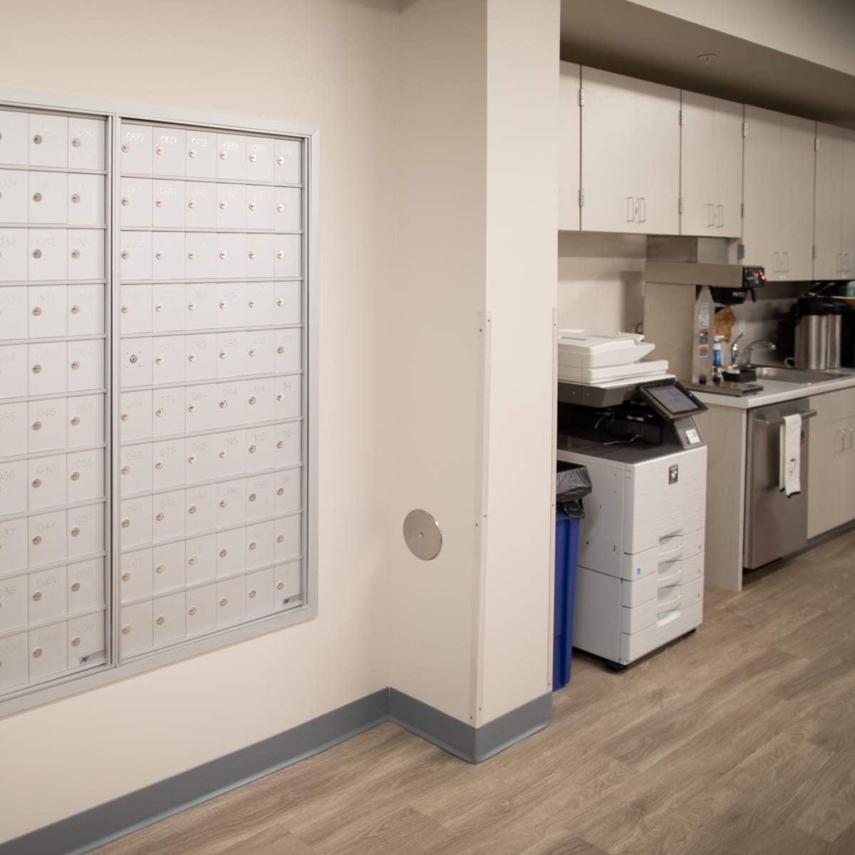A mail delivery area featuring a wall-mounted mailbox unit and an adjacent kitchen space with a photocopier and coffee machine.