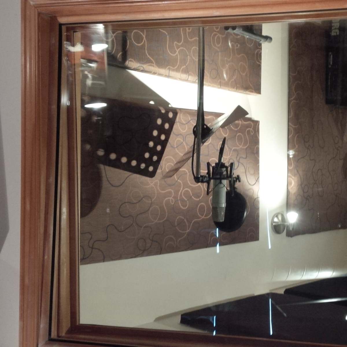 A recording studio with a microphone suspended in front of sound-absorbing panels, viewed through a wooden-framed window.