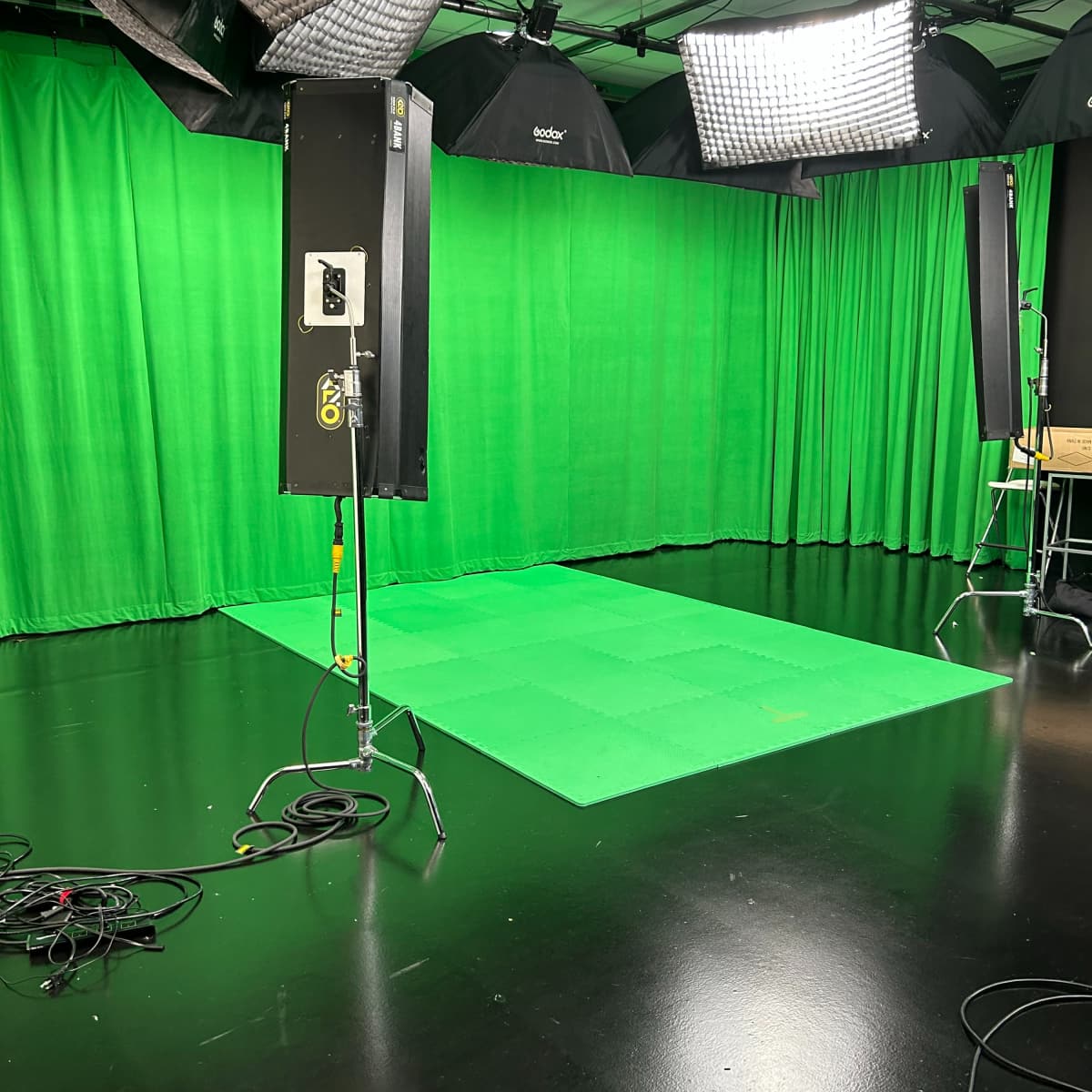 A studio is set up with green curtains and a green floor for use in video production.