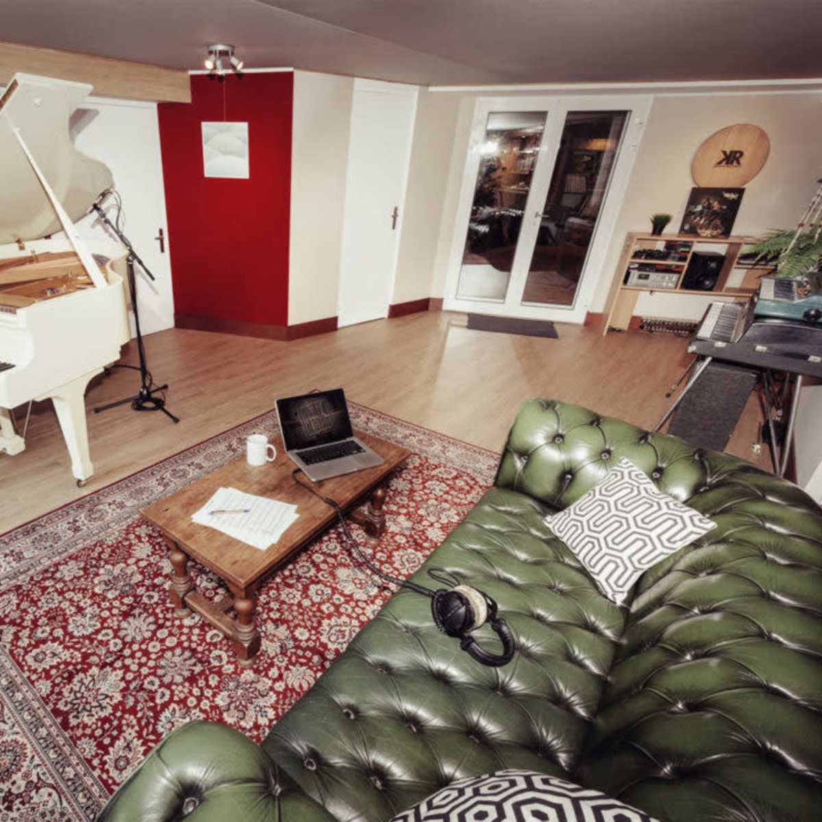 A music room featuring a white grand piano, a green leather sofa, a wooden coffee table, and a laptop on the floor.