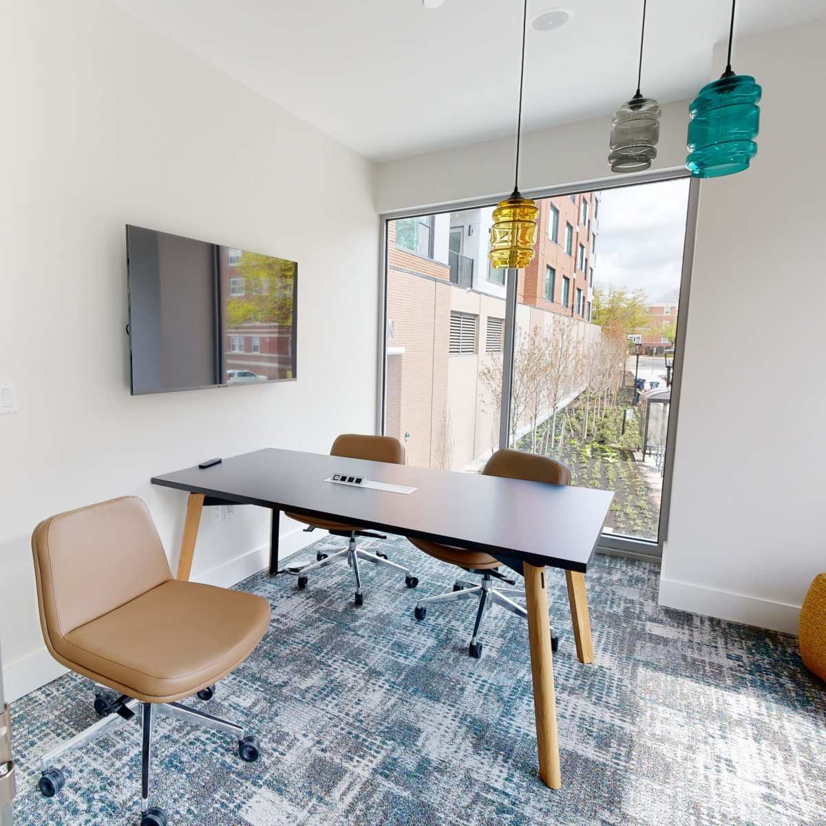 A modern meeting room with a table, chairs, and a TV, featuring large windows and colorful pendant lights.