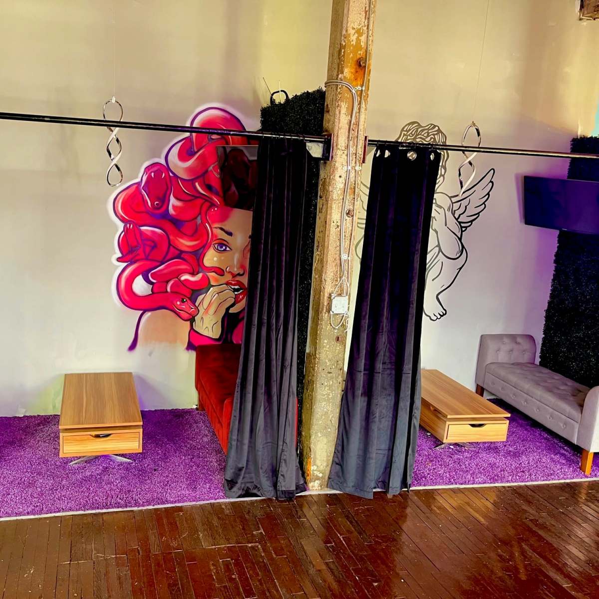 A lounge area featuring two seating sections with colorful walls, a vibrant mural, and curtains separating the spaces.