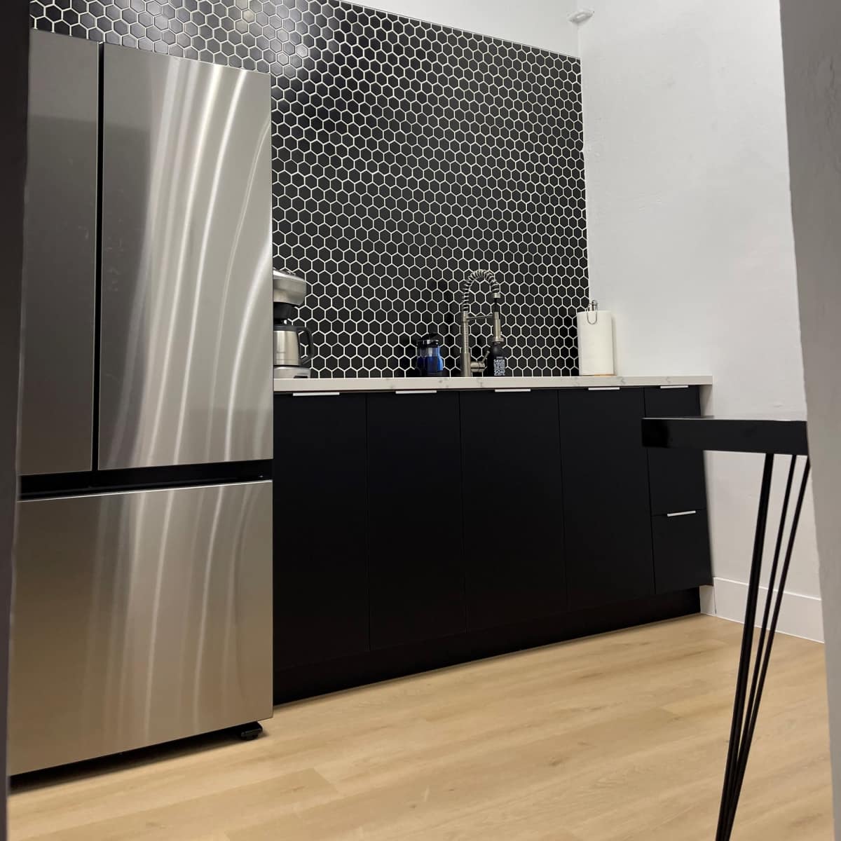 A modern kitchen features a stainless steel refrigerator, black cabinetry, and a hexagonal tile backsplash.