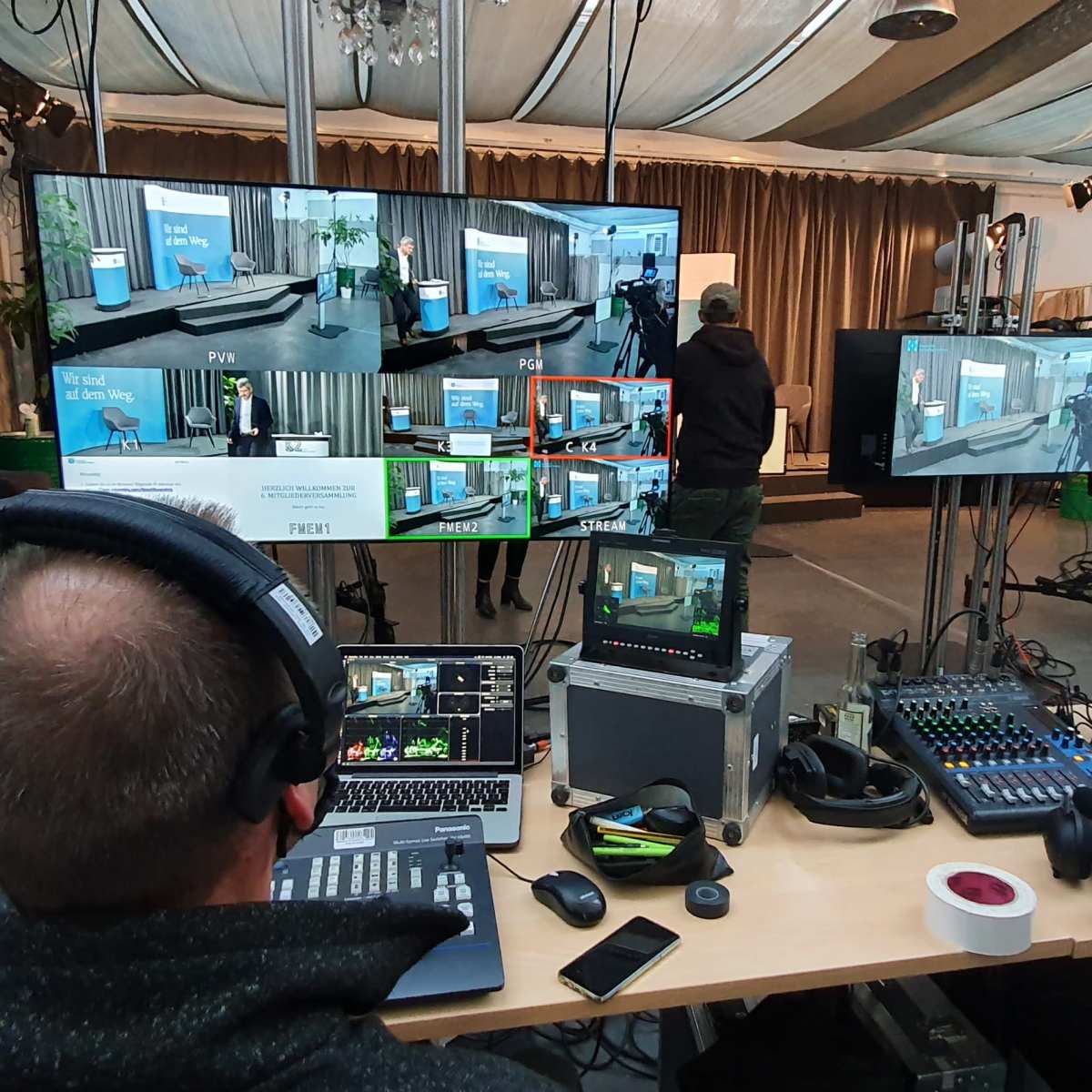 A man operates audio-visual equipment at a control station with multiple screens in a studio setting.