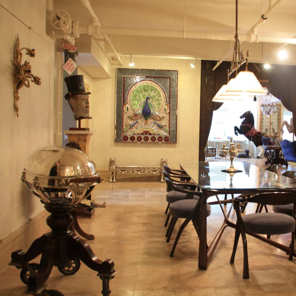 A modern dining area with a glass table surrounded by chairs, sculptures, and a large decorative clock on the wall.