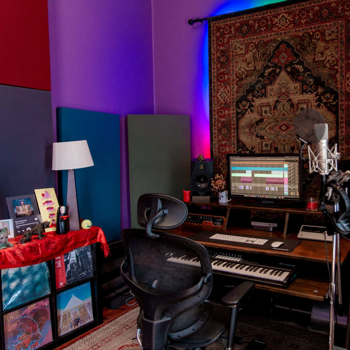 A music production studio features a microphone in front of a computer setup, surrounded by soundproofing panels and decorative lighting.