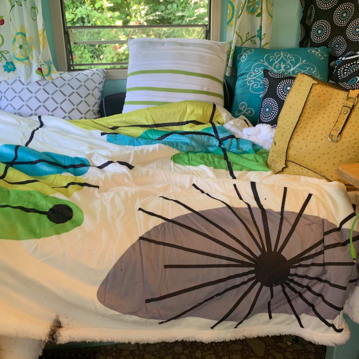 A colorful bedding spread with leaf patterns covers a couch surrounded by decorative pillows and a yellow bag.