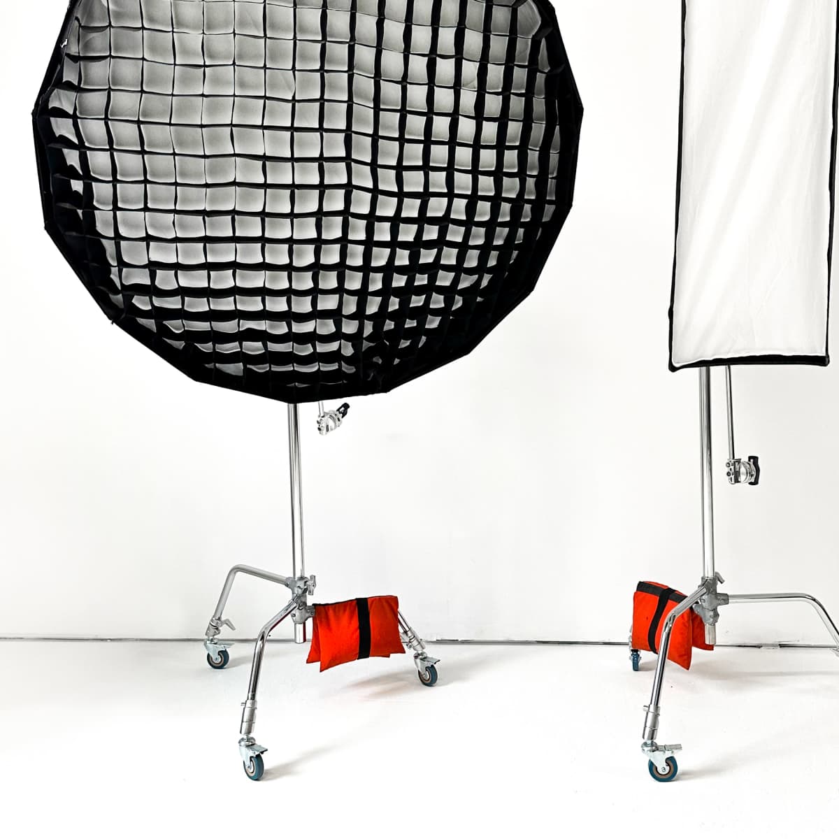 Two wheeled light modifiers, one with a black grid and the other with a white fabric, positioned against a white backdrop.