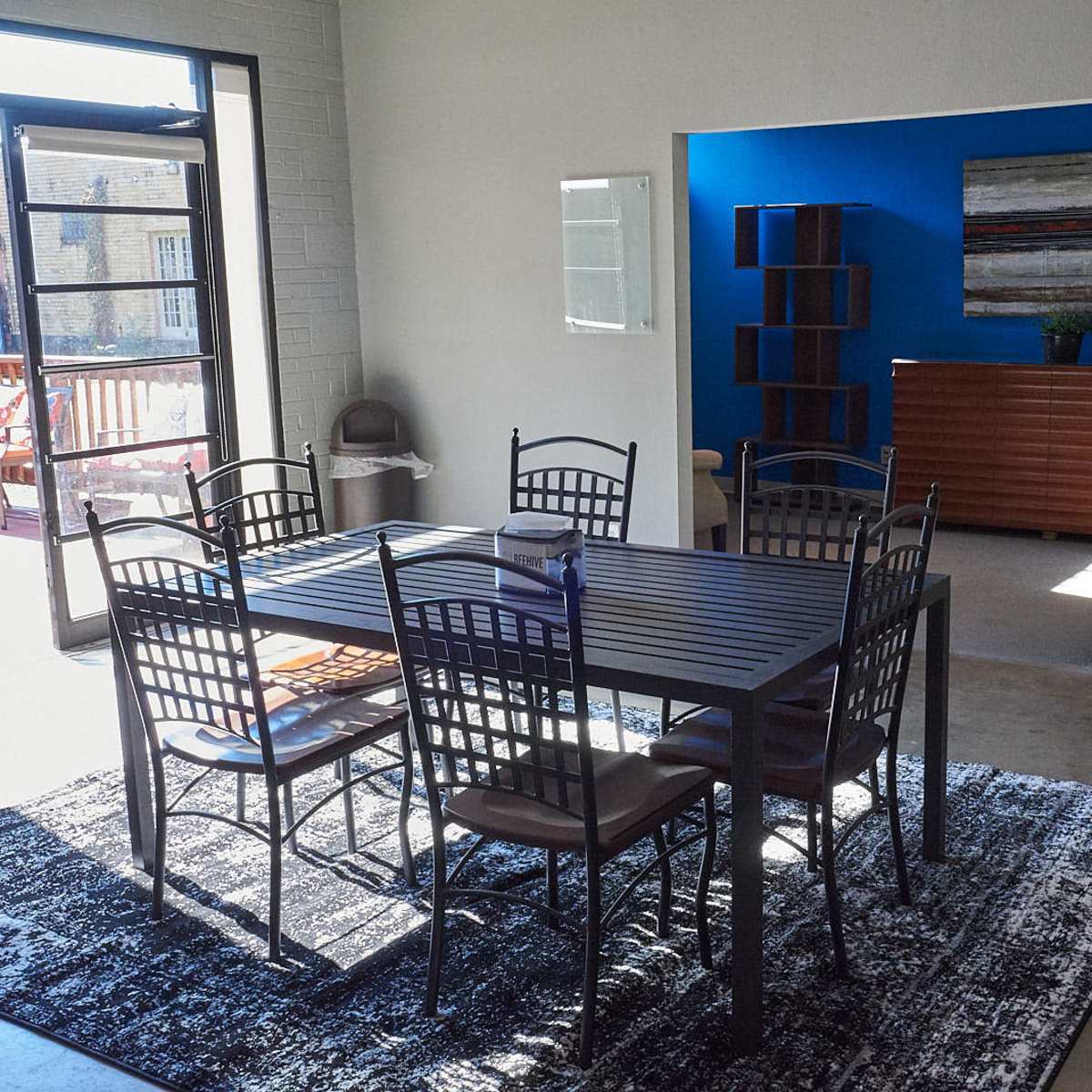 A modern dining area with a black rectangular table surrounded by six metal chairs, next to a large window and a blue-accented wall.