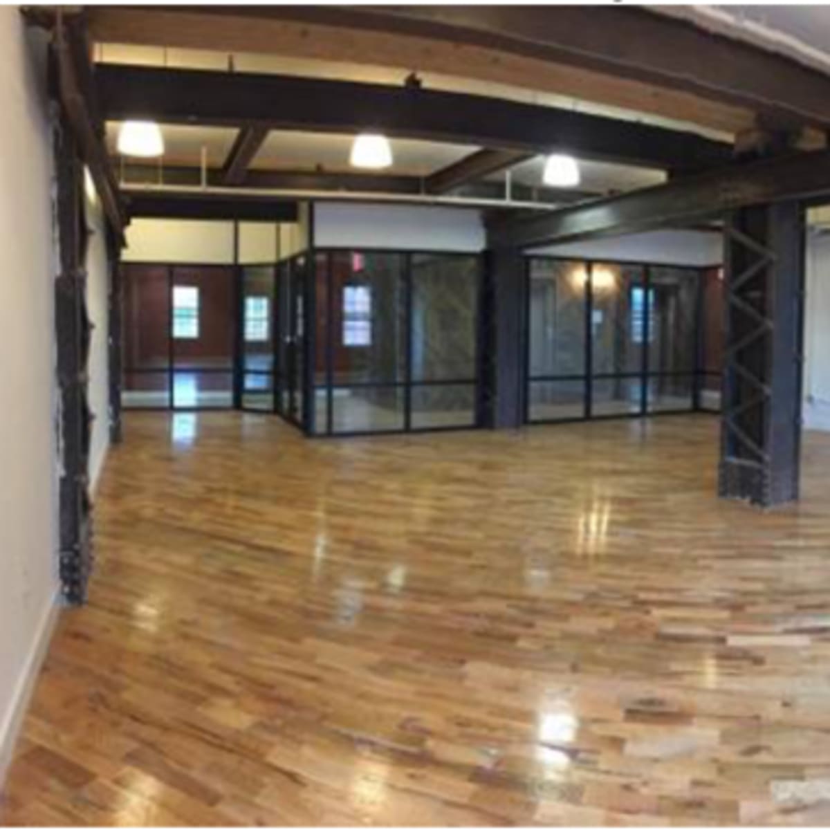 An open room with polished wooden floors, exposed beams, and a glass-walled section in the center.