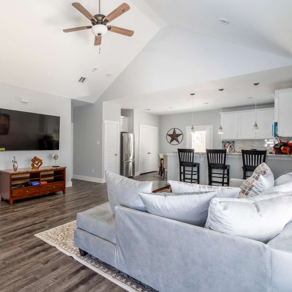 A modern living room featuring a gray sofa, a wooden TV cabinet, and an open kitchen area with bar seating.