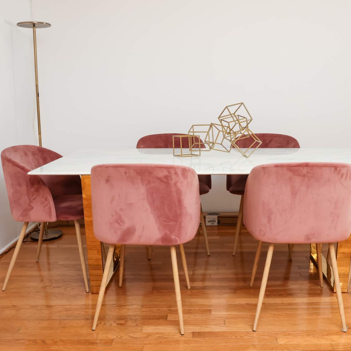 A rectangular dining table with a marble top is surrounded by six pink velvet chairs, and a decorative geometric sculpture sits in the center.
