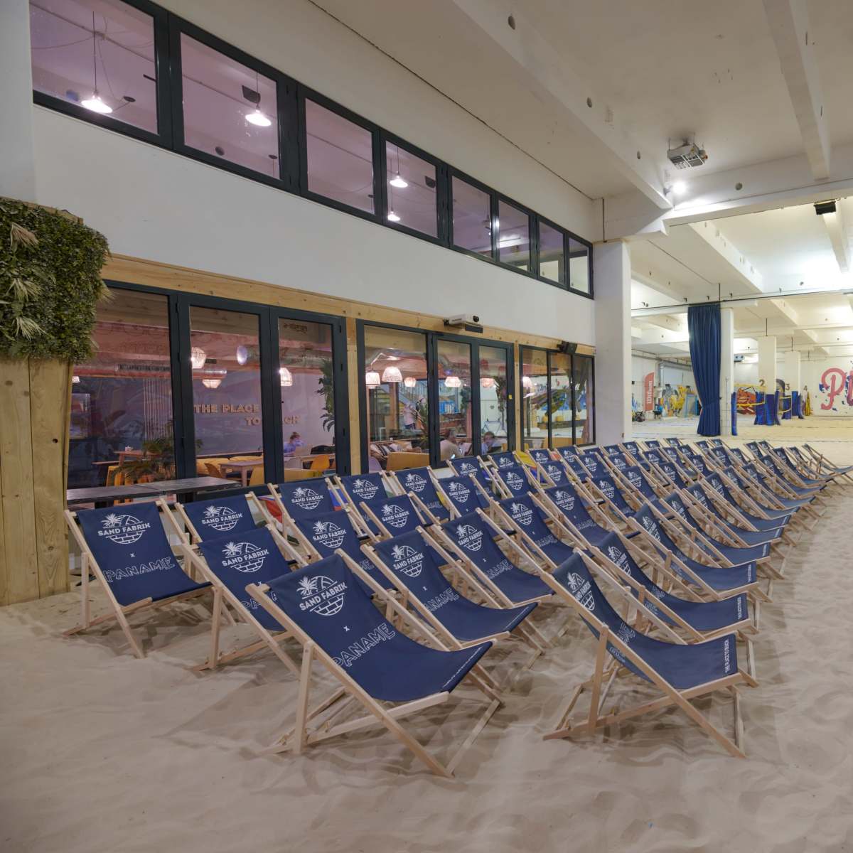 A room with chairs arranged in rows on sand, surrounded by colorful murals and large windows.