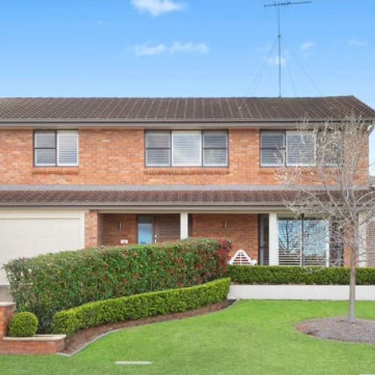 A two-story brick house with a neatly landscaped front yard and a paved driveway.