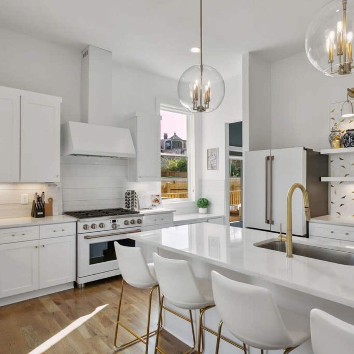 A modern kitchen features white cabinetry, a large island with four bar stools, and decorative wall tiles.