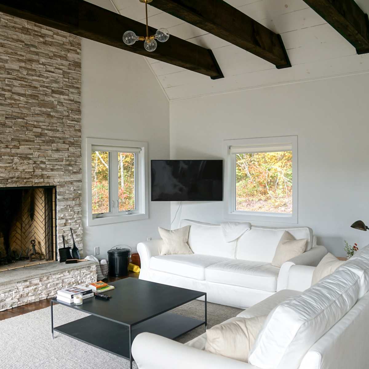 The living room features a stone fireplace, white sofas, a black coffee table, and large windows that offer natural light.