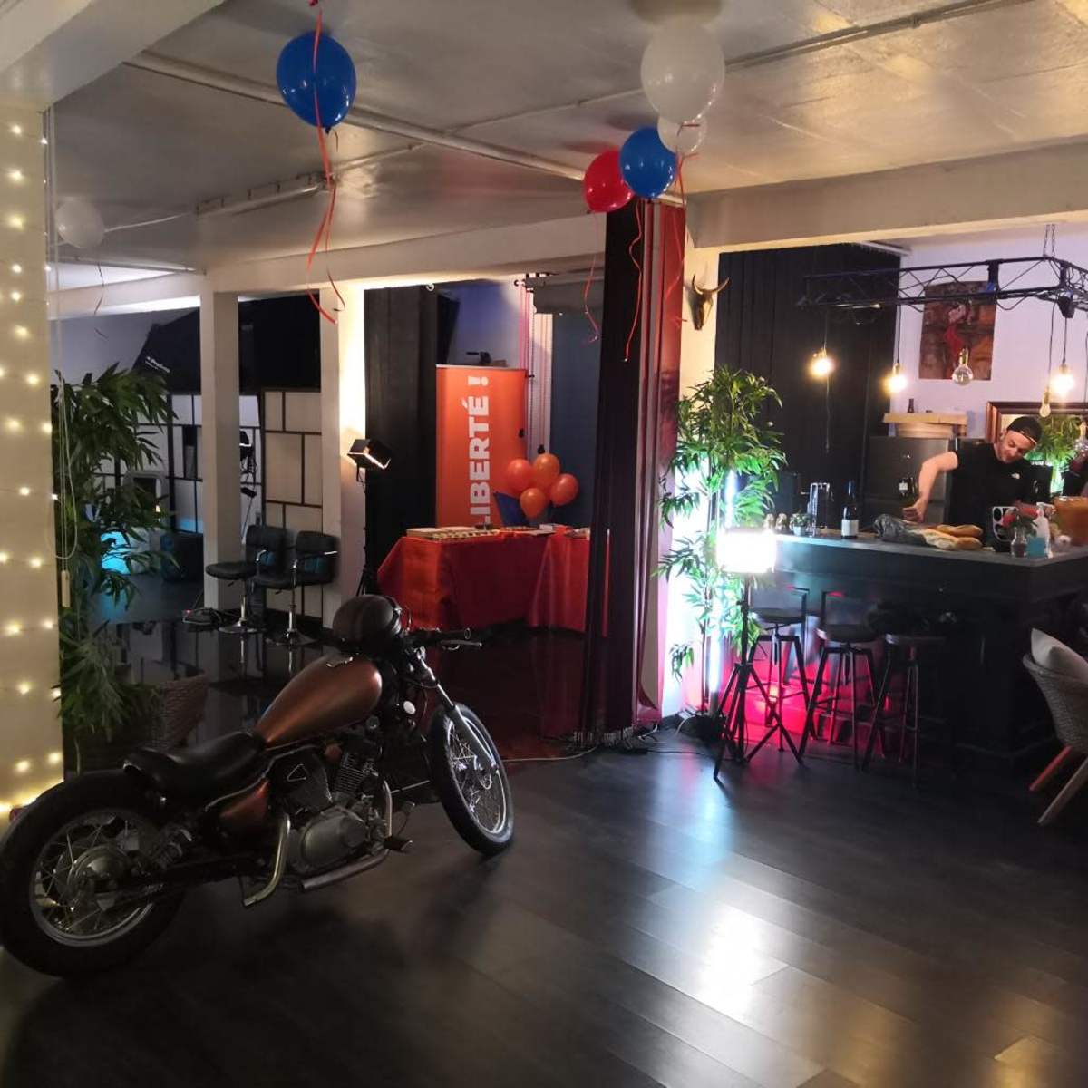 A decorated indoor space featuring a motorcycle, a bar setup with lights, and festive balloons.