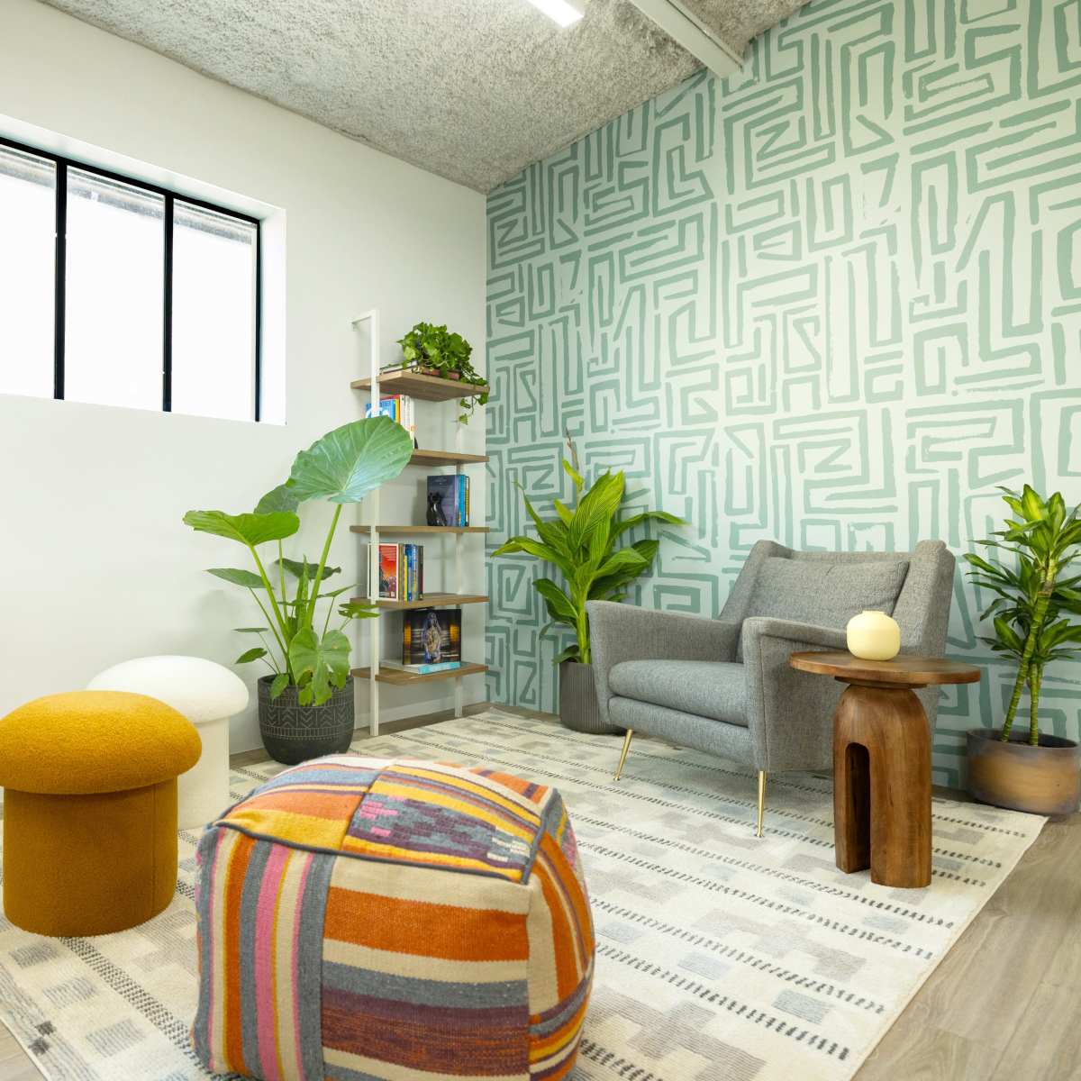 A modern, inviting room with a patterned accent wall, a gray armchair, potted plants, and colorful decorative elements.