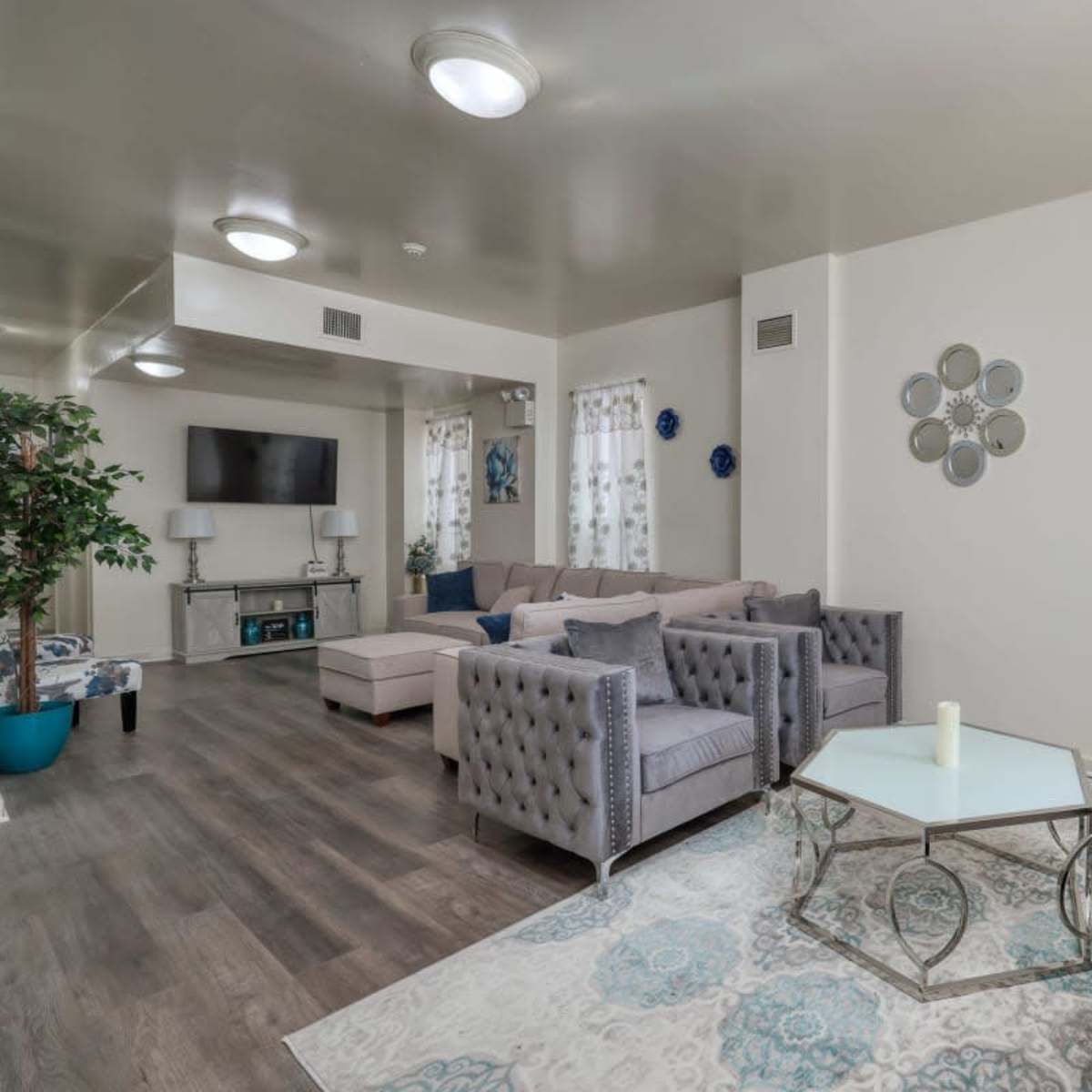 A modern living room with gray upholstered furniture, a light-colored coffee table, and a large television mounted on the wall.