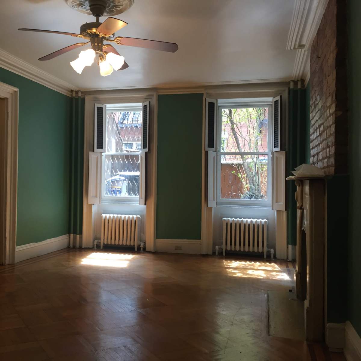 A room with green walls, two windows, a ceiling fan, and a fireplace.
