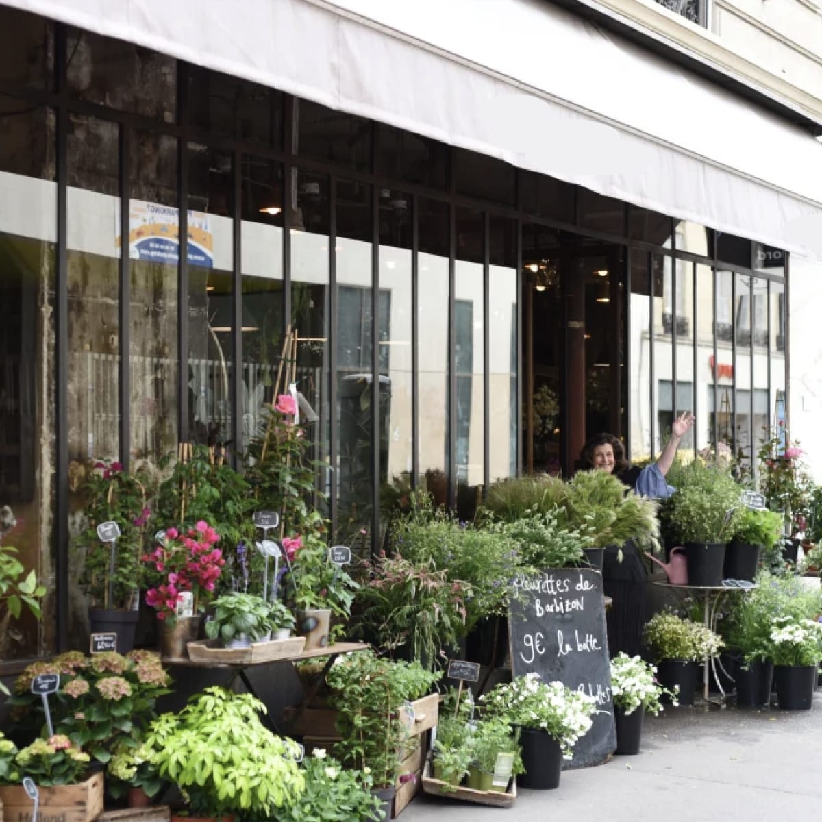 A storefront displays a variety of potted plants and floral arrangements under a canopy.