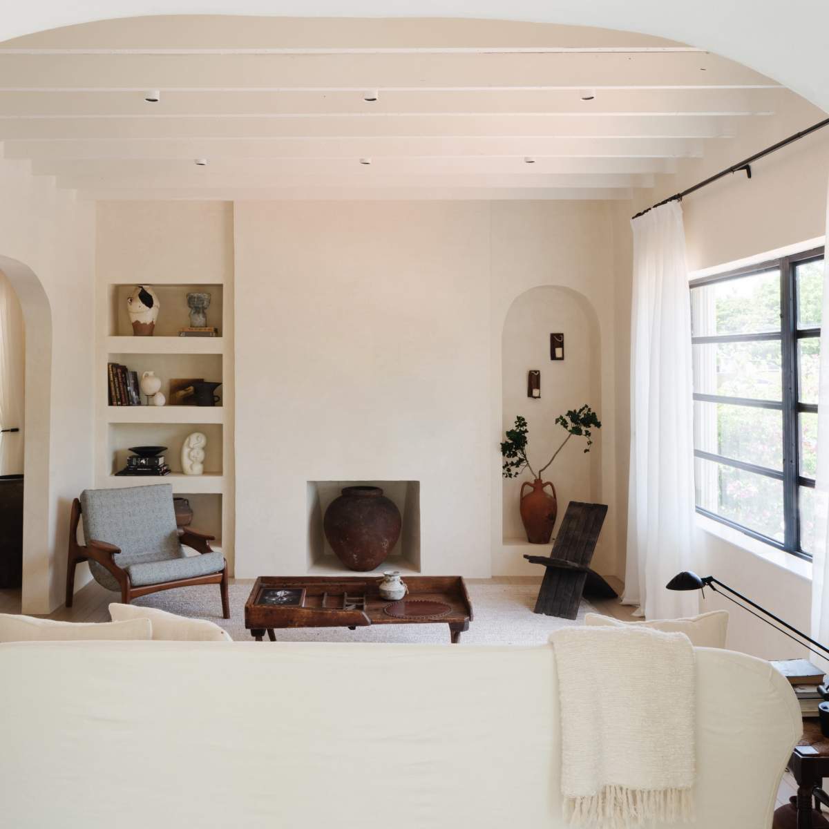 A minimalist living room with a sofa facing a coffee table, surrounded by shelves and decor items.