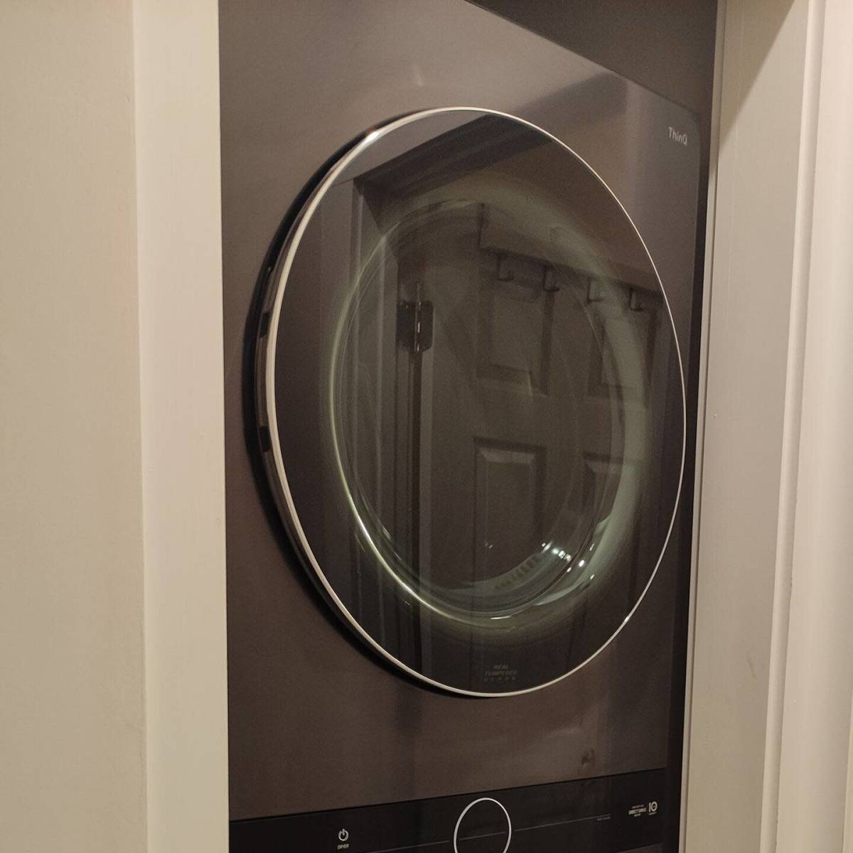 A stacked washer and dryer unit in a narrow space with a dark finish and circular doors.