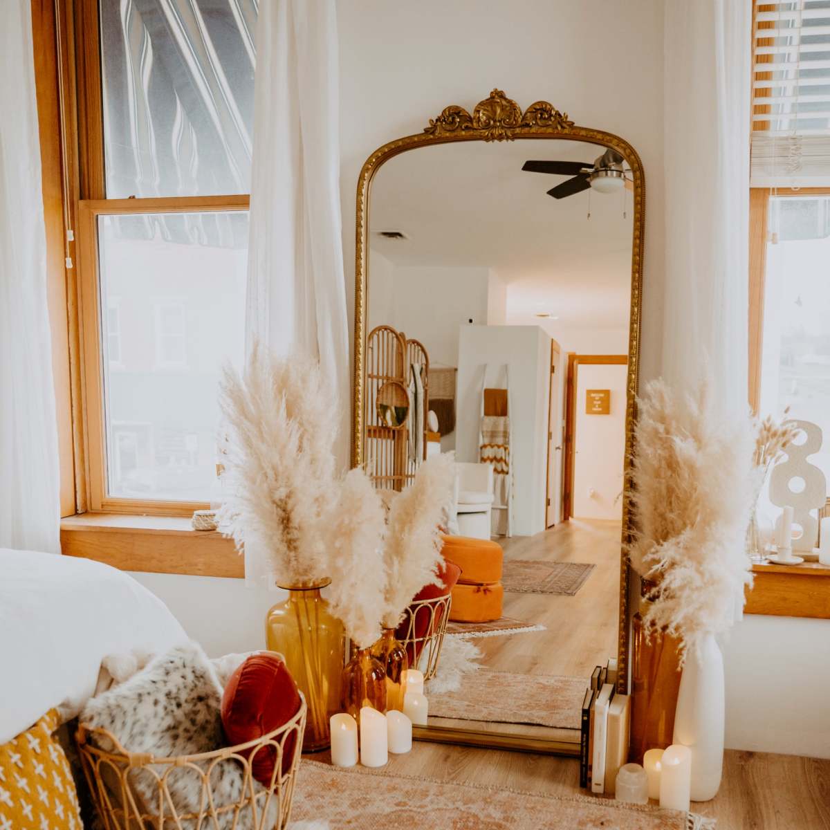A room with a large ornate mirror surrounded by decorative vases filled with pampas grass and several candles on the floor.