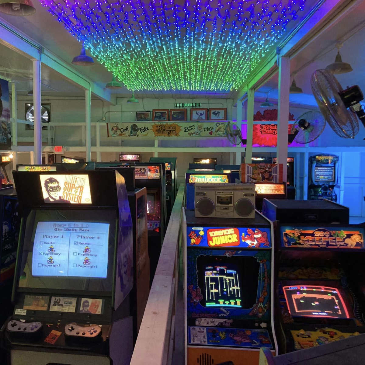 A retro arcade filled with various classic video game machines under a colorful, illuminated ceiling.