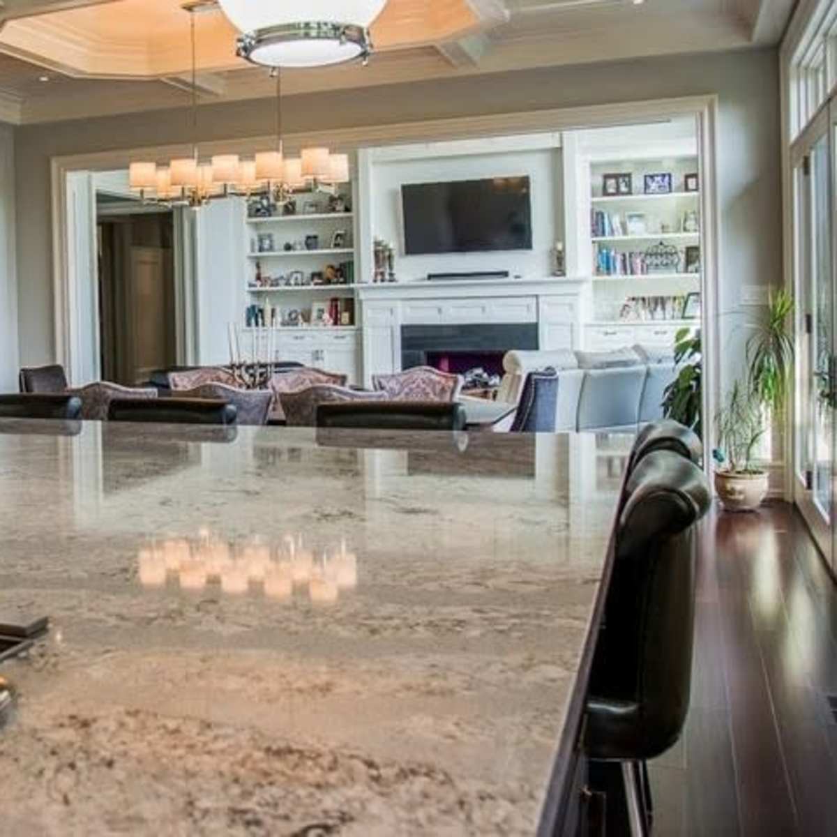 A spacious kitchen features a large granite countertop with a stovetop, and a living area with a television and bookshelves is visible in the background.