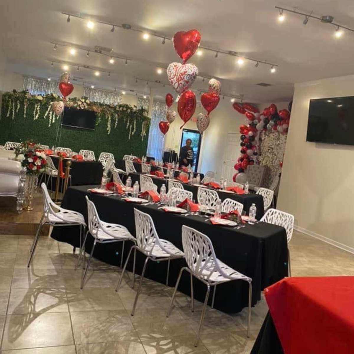 A decorated event space with black tables set for dining, adorned with red and silver balloons and floral arrangements.