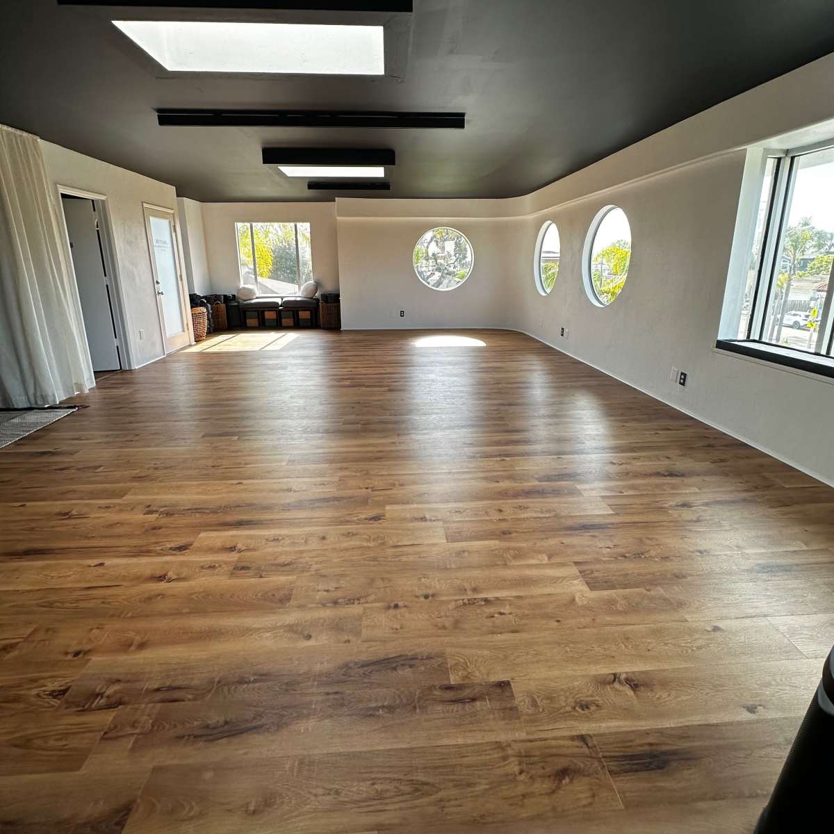 A spacious room with light wooden flooring and circular windows, featuring a dark ceiling and minimal furnishings.