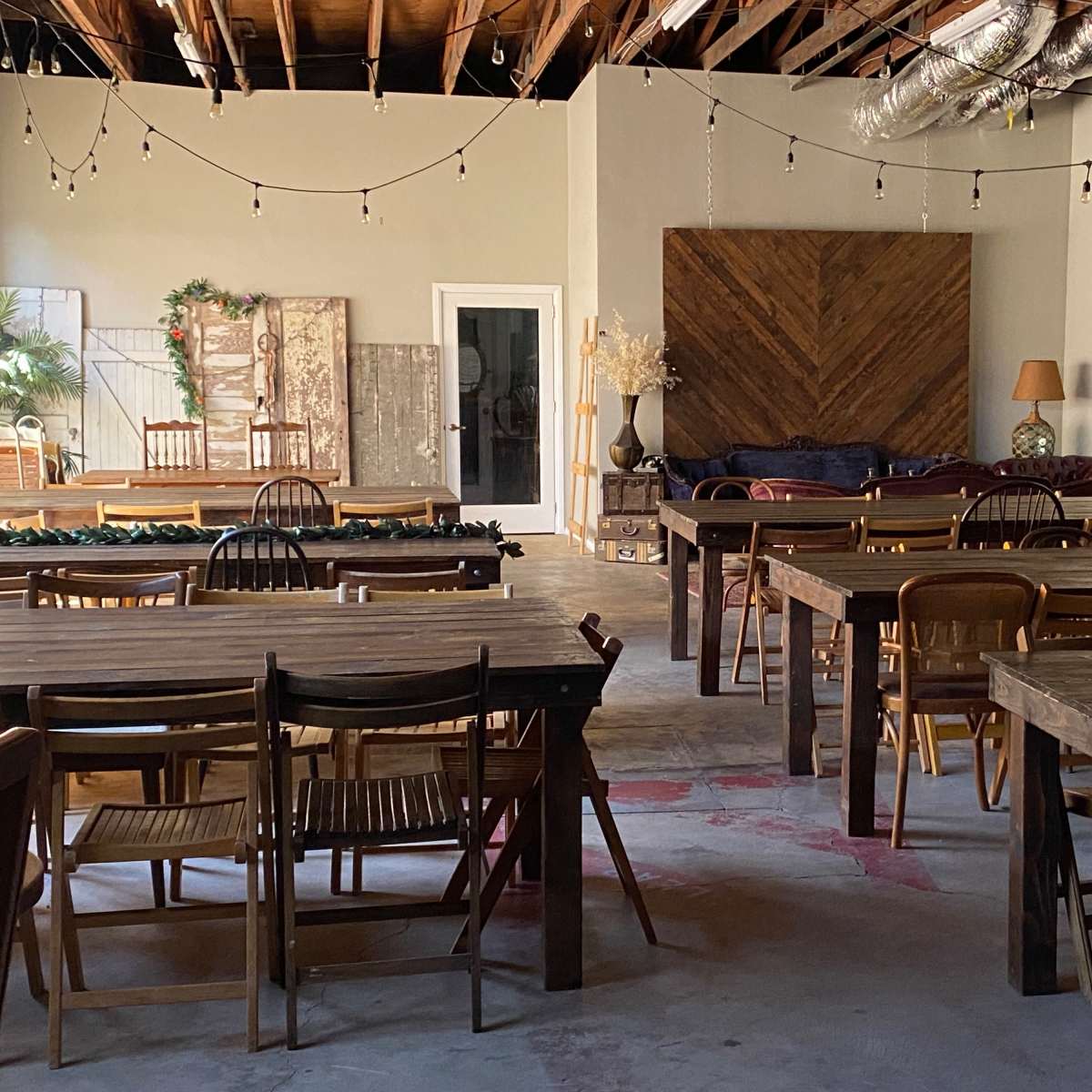 A spacious, well-lit room with wooden tables and chairs arranged for an event, featuring a cozy seating area and decorative elements on the walls.