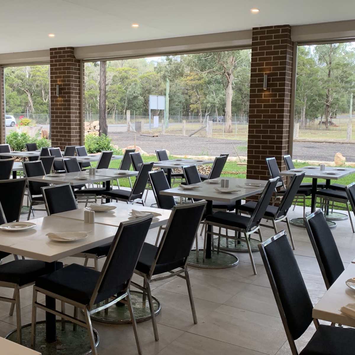 A spacious dining area with gray tables and chairs arranged neatly, surrounded by large windows overlooking a green landscape.