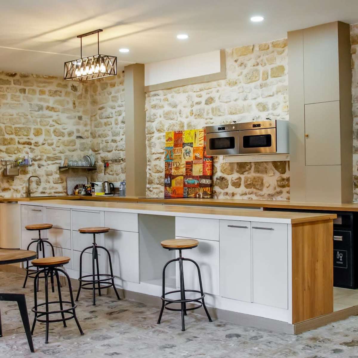 A modern kitchen with a stone wall, a long wooden countertop, and several bar stools.