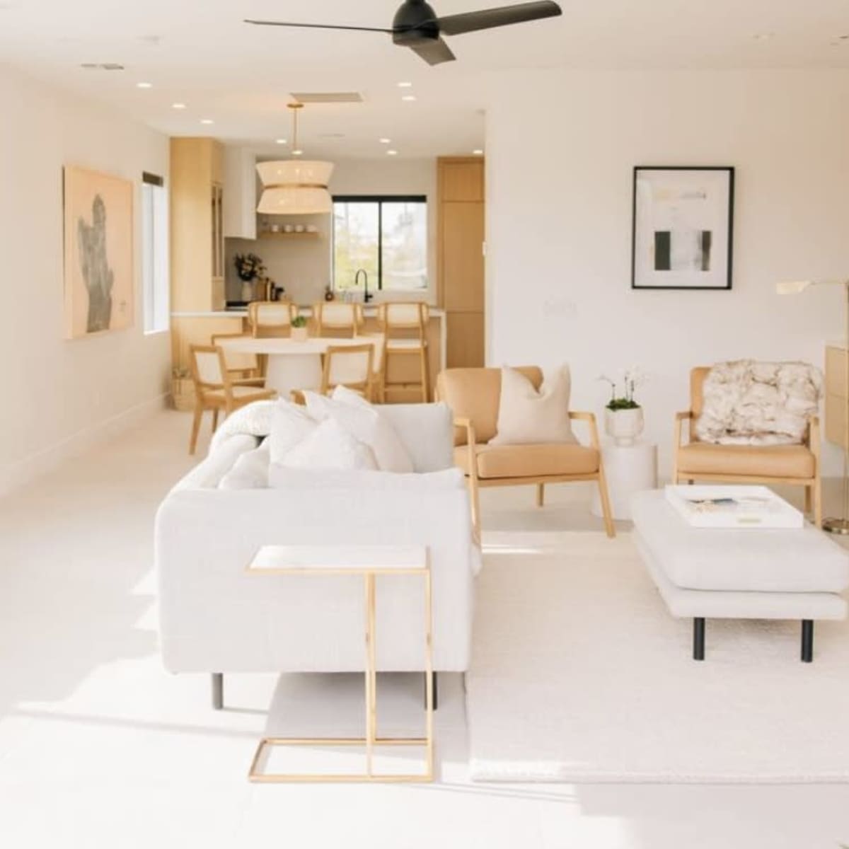 A modern living room with a light color palette, featuring a sectional sofa, armchairs, a coffee table, and a dining area in the background.