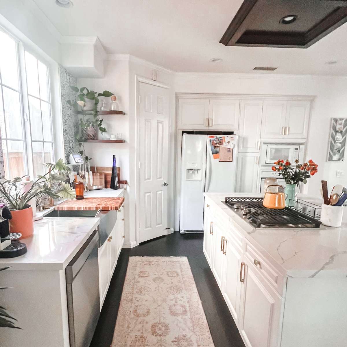 A modern kitchen with white cabinets, a gas stove, and a sleek countertop, featuring plants and a neon sign that says "Hustle."