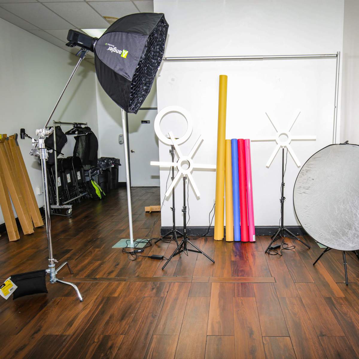 A photography studio setup featuring a softbox light, several background rolls, and a reflector on a wooden floor.