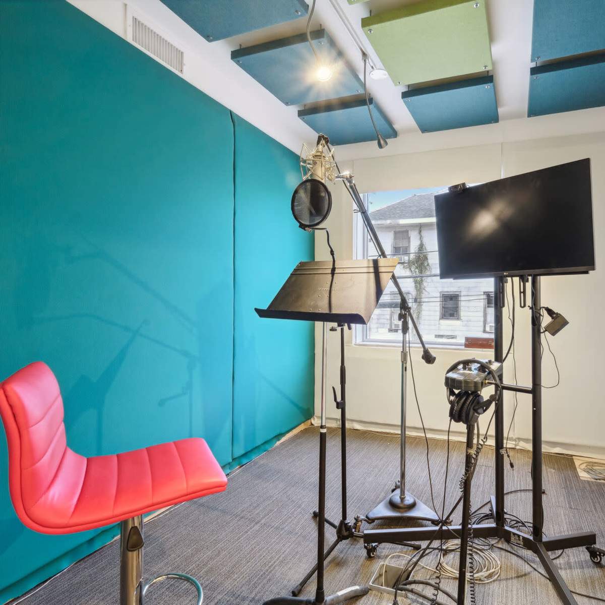 A small recording studio with a red chair, a microphone setup, a music stand, and a monitor.