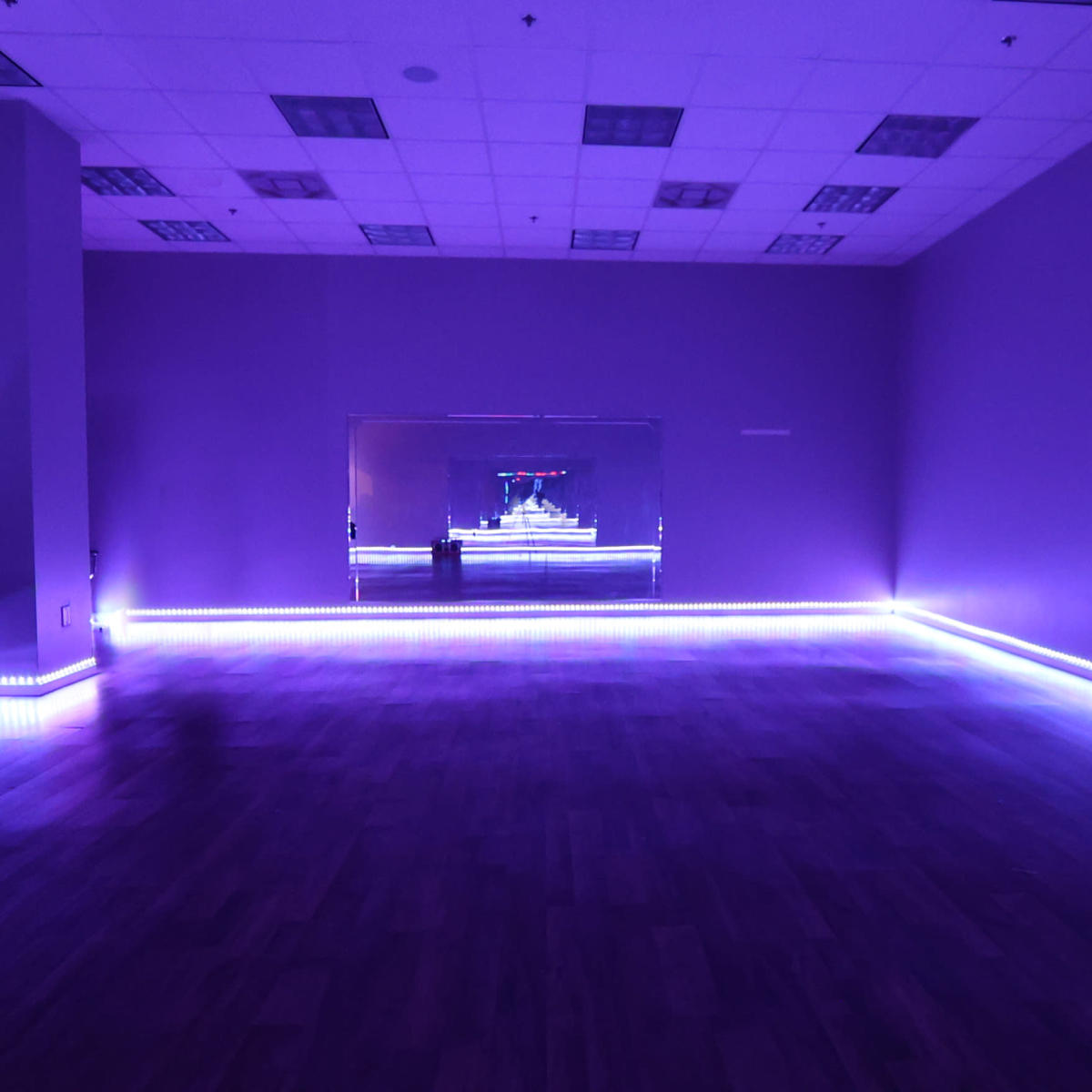 A spacious room with purple walls and ambient lighting features a mirrored wall and wooden flooring.